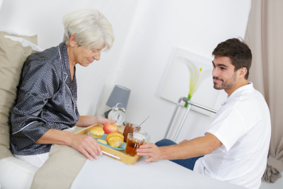 caregiver serving breakfast in bed to senior woman