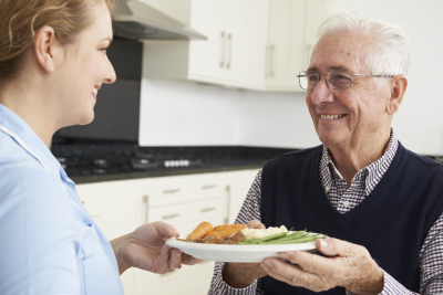 caregiver serving food to senior man